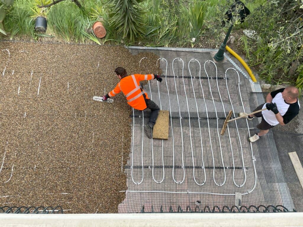 An installer carefully applying a resin-bound surface over an existing block paving driveway, ensuring a smooth and durable finish.